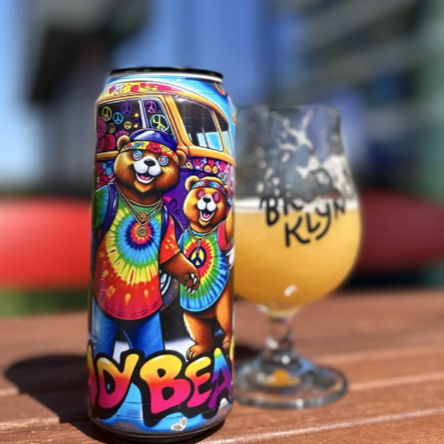 DankHouse Deady Bears Colorful beer can with bear design next to a glass of beer on a wooden surface